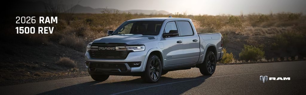A 2026 RAM 1500 REV electric truck driving on a desert road with mountains in the background.