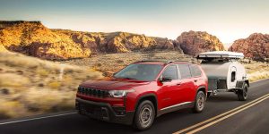 A red Jeep SUV towing a small trailer on a road.